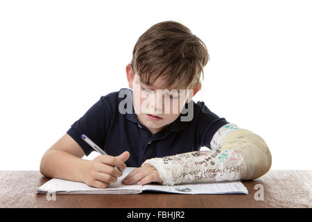 kleiner Junge studiert hart, während er einen gebrochenen linken Arm hat seine Hausaufgaben Stockfoto