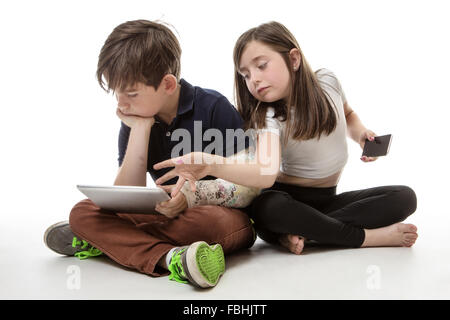 Zwei Kinder sitzen nebeneinander, während das Spiel mit einem Mobiltelefon und einem Tablet-computer Stockfoto