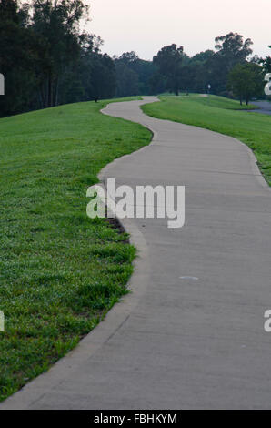 Ein gewundener, betonierter Wander- oder Radweg auf einem kleinen Hügel mit Gras auf beiden Seiten Stockfoto