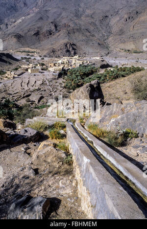 Wadi Bani Kharus, Oman. Bewässerungskanal (Falaj) Führt Wasser am Berghang hinunter zum Dorf und Dattelpalmen darunter. Stockfoto