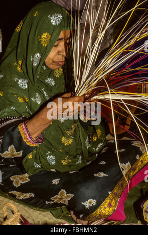 Qurum, Oman.  Frau mittleren Alters mit Stroh, einen Korb zu machen.  Muscat Festival, traditionelles Handwerk zu demonstrieren. Stockfoto