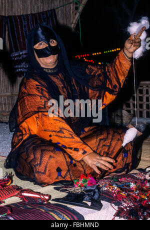 Qurum, Oman.  Frau mittleren Alters maskierte Faden aus Wolle spinnen.  Muscat Festival, traditionelle omanische Handwerkskunst demonstriert. Stockfoto