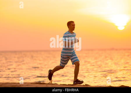 Gesunde Lebensweise: hübscher junger Mann arbeiten im Freien, läuft schnell auf Sand Ufer bei Sonnenauf- oder Sonnenuntergang Stockfoto