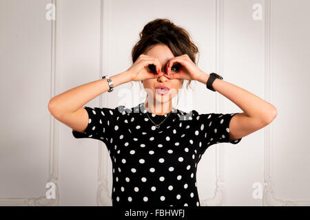 Porträt von schöne Brünette Frau in einem schwarzen Kleid, die durch ihre Hände wie Fernglas suchen Stockfoto