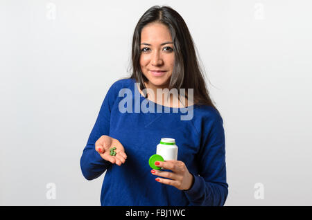 Grinsend selbstbewusste junge Frau im blauen Pullover über isoliert Hintergrund grüne Tabletten in der Hand halten Stockfoto