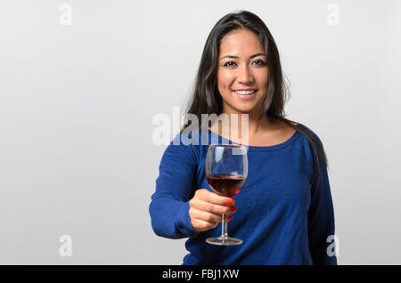 Glücklich attraktive junge Frau mit einem Glas Rotwein an der Kamera erhöhen, da sie einen besonderen Anlass feiert Toasten Stockfoto