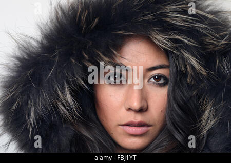 Hübsche junge Frau in einem pelzigen Kapuze schaut direkt in die Kamera mit einem ernsten Ausdruck konzeptionelle Wintermode und bea Stockfoto