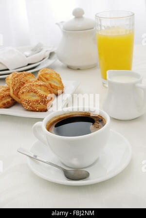 Tasse Kaffee mit frisch gebackenen Brötchen mit Sesam, Saft und Milch am Morgen Stockfoto