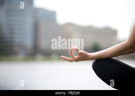 Nahaufnahme der Hände der jungen Büro Yogi Frau Schneidersitz im Yoga einfach Sukhasana posieren am Flussufer in der Stadt, Schneidstoffe Stockfoto