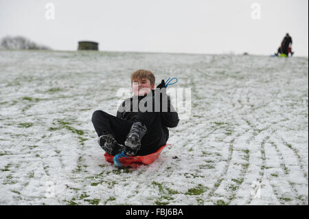 Ein Junge rutscht einem Schnee - covered​ Hang auf einem Schlitten in Clayton, East Sussex, UK. Stockfoto