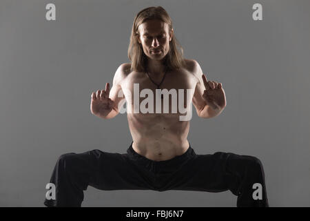 Porträt der sportliche junge Mann in schwarz Hose tun Yoga-Pose, stehend im Rudrasana (Sumo), Utkata Konasana (Göttin zu stärken Stockfoto