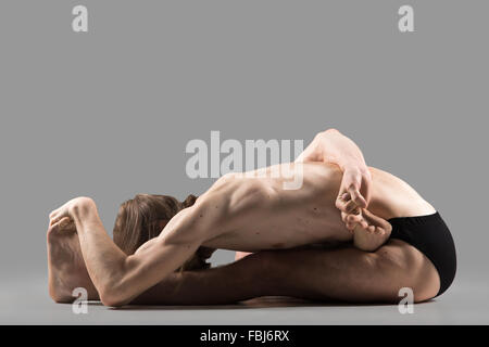 Sportlich muskulösen jungen Yogi Mann mit langen Haaren sitzen im Ardha Baddha Padma Paschimottanasana, halb gebunden Lotus nach vorne beugen pos Stockfoto