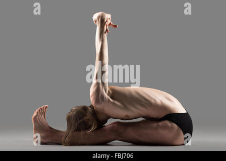 Sportlich muskulösen jungen Yogi Mann sitzt in Variation der Paschimottanasana, sitzend nach vorne beugen Haltung mit Arme gestreckt hinter Stockfoto