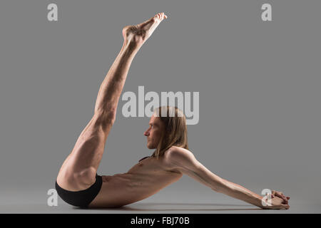 Sportlich muskulösen jungen Yogi Mann Übungen für Bauchmuskeln und Schultern, Beine, hob Studio gedreht auf dunklen Stockfoto