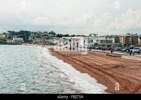 Urlauber schlendern Sie entlang der konkreten Promenade wie Schaumkronen auf den Kämmen des kleinen brechenden Wellen Schaum auf dem roten Sand verlassen Stockfoto