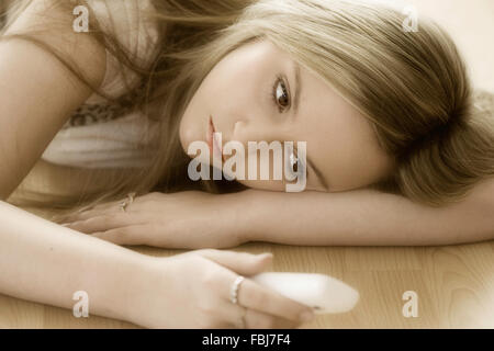 Schöne junge Frau, 16 Jahre alt, Kopf und Schultern, blond, blaue Augen, mit traurigen Ausdruck, Telefon, während am Boden. Soft Focus Stockfoto