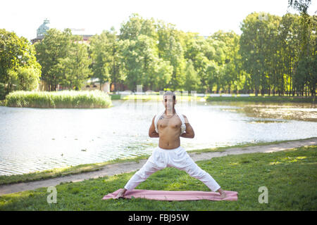 Attraktive indische junger Mann in weißem Leinen Kleidung am Ufer des Flusses im Park trainieren tun Vorbereitung für Pyramide darstellen, Intens Stockfoto