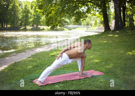 Sportlich asiatische junger Mann in weißen Sportswear auf dem Rasen im Park trainieren dabei Yoga, Fitness, Pilates Training, niedrige Longe Caravans Stockfoto