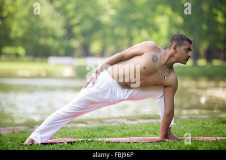 Sportlich asiatische junger Mann in weißen Sportbekleidung trainieren auf dem Rasen im Park, beim Yoga, Fitness, Pilates training, niedrige Longe zu tun Stockfoto