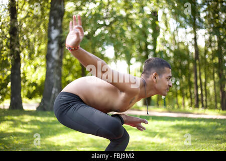 Sportlich schöne indische junger Mann Training im Park, halben Lotus Tip Toe darstellen, Ardha Baddha Padma Padangusthasana vorbereiten, Stockfoto