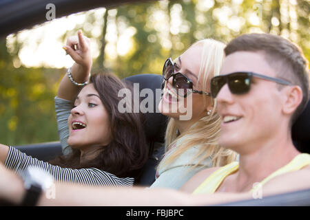 Gruppe von drei unbeschwerten fröhlichen Freunden auf Urlaub, Sommertag im Cabrio unterwegs, gemeinsam Spaß haben Stockfoto