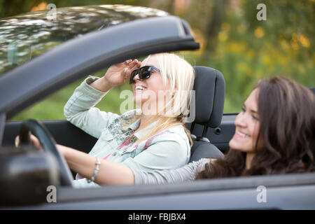 Zwei junge Frauen, die schönen fröhlichen Reisenden Reiten Sportwagen, Fokus auf unbeschwerte Lachen Passagier blondes Mädchen in Sonnenbrillen und Stockfoto