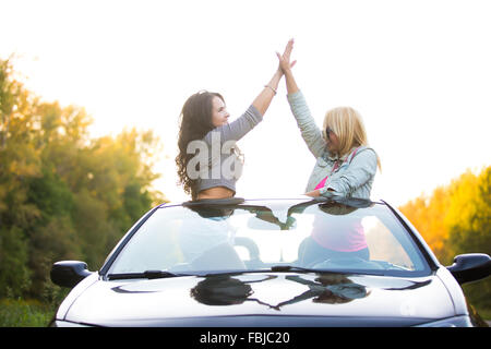 Zwei glückliche Freunde fahren moderne Luxus-Cabrio-Auto im Urlaub auf Sommertag. Schöne fröhliche junge Damen geben hohe fiv Stockfoto