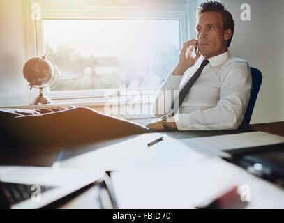 Wieder zuversichtlich Geschäftsmann sitzt an seinem Schreibtisch mit Füßen, spricht am Telefon mit Dokumenten auf seinem Schreibtisch gelegt Stockfoto