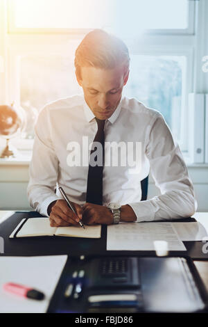 Weißen männlichen Exekutive arbeiten im Büro am Schreibtisch mit Konten und Dokumente, auf der Suche in einem schwarzen Notizbuch Stockfoto