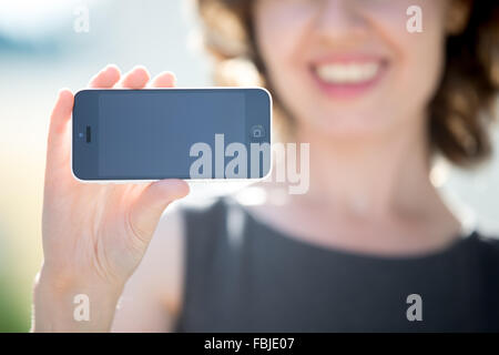 Glücklich lächelnde junge Frau zeigt leere schwarze Touchscreen-Display auf Smartphone auf der Straße. Fokus auf leeren Eingabemaske für Kopie sp Stockfoto