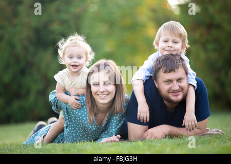 Mutter, Vater und zwei Kinder auf dem Rasen im Park liegen. Porträt der glückliche schöne Familie von vier auf Wiese entspannen, Spaß zu haben Stockfoto