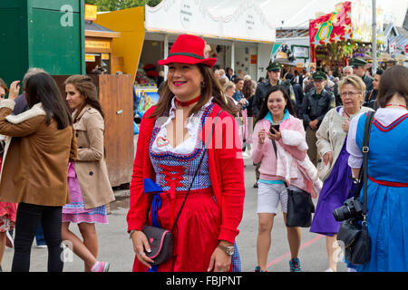 Lächelnde junge Frauen tragen Dirndl und Tiroler Hut zu Fuß durch die Menschenmenge auf dem Oktoberfest in München, Deutschland Stockfoto