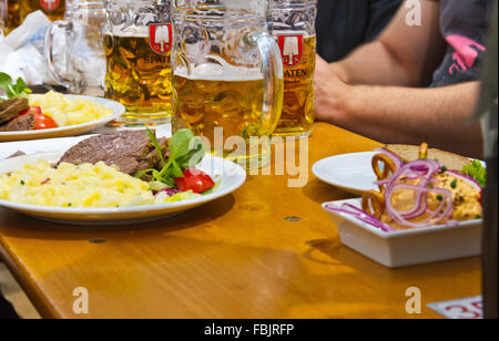 Teller und Becher Bier auf einem Tisch in einer Bierhalle auf dem Oktoberfest in München. Stockfoto