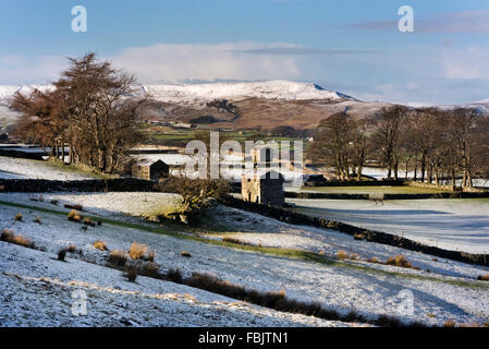 Traditionelle Yorkshire Dales Scheunen mit der Markt-Stadt Hawes und eine verschneite Widdale fiel darüber hinaus, North Yorkshire, UK. Stockfoto