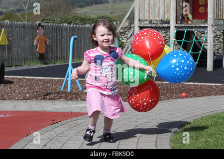 Kleines Mädchen laufen und spielen mit Luftballons in einer Gärtnerei, Spaß Stockfoto