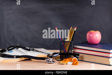 Desktop mit Stethoskop, Medizin Pillen, Bücher, Stifte, Apfel, Lesebrille und leere Tafel im Hintergrund. Stockfoto