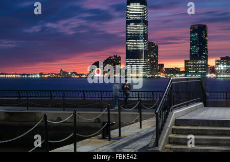 Lange Exposition Blick auf den Sonnenuntergang mit World Financial Plaza und zwei Männer stehen und Jersey City Türme im Hintergrund. Stockfoto