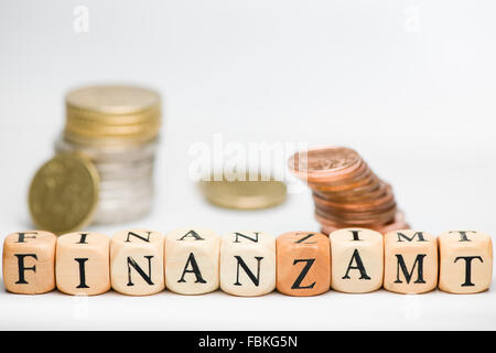 Eine Reihe von Buchstaben Würfeln das deutsche Wort "Finanzamt" (Finanzamt) vertritt und kleine fuzzy gestapelten Münzen auf weiß Stockfoto