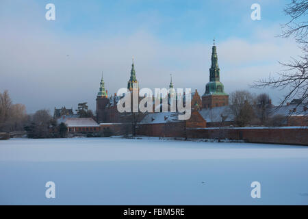 Schloss Frederiksborg an einem Wintertag. Schnee auf zugefrorenen Schlossteich. Die Sonne bricht durch den frostigen Nebel. Von SE betrachtet. Stockfoto