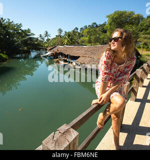 Tourist-Frau sitzt auf der Brücke über den Fluss in Asien. Stockfoto