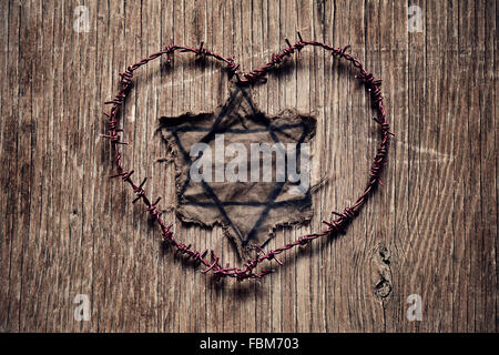Nahaufnahme eines jüdischen Abzeichen und Stacheldraht bilden ein Herz auf eine rustikale Oberfläche, in Gedenken an die Opfer des Holocaust Stockfoto