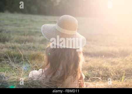 Rückansicht des ein Mädchen sitzt in einem Feld Stockfoto