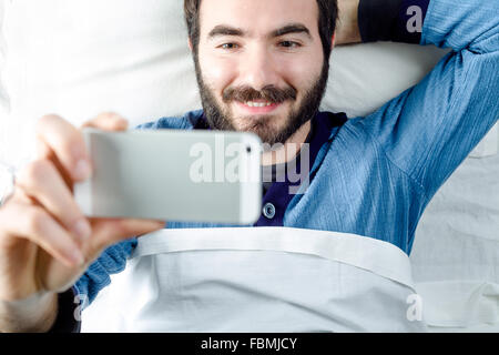 Lächelnder Mann mit Pyjamas, wobei ein Selbstporträt mit einem Smartphone Stockfoto