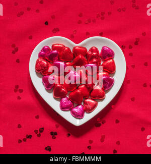 Eine herzförmige Platte voller valentine Pralinen auf einem roten Hintergrund. Blick von oben nach unten schaut. Stockfoto