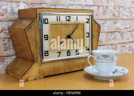 Hölzerne Mantel Vintage Art-déco-Uhr mit alten Ziegel Wand Effekt Hintergrund und China Teetasse und mit Tee gefüllt Stockfoto