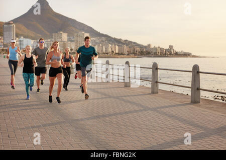 Gesunde junge Menschen, die entlang der Küste. Club-Gruppe Lauftraining zusammen auf einem Steg am Meer in der Stadt. Stockfoto