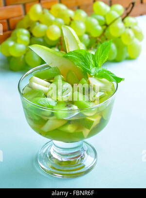 Obstsalat mit Trauben, Kiwi, Birnen, garniert mit Wein im Glas, dekoriert mit Minze. Stockfoto