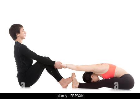 Zwei sportliche Menschen praktizieren Yoga, stretching Mädchen im sitzen nach vorne beugen Pose, Paschimottanasana mit Hilfe Stockfoto