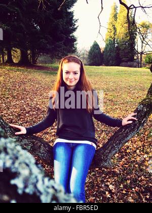 Porträt der glückliche junge Frau sitzend auf Ast im Park