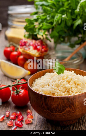 Couscous, gekocht frisches Gemüse für Salat: Tomaten, Granatapfel, Zitrone, Petersilie und Olivenöl auf einem hölzernen Hintergrund Stockfoto